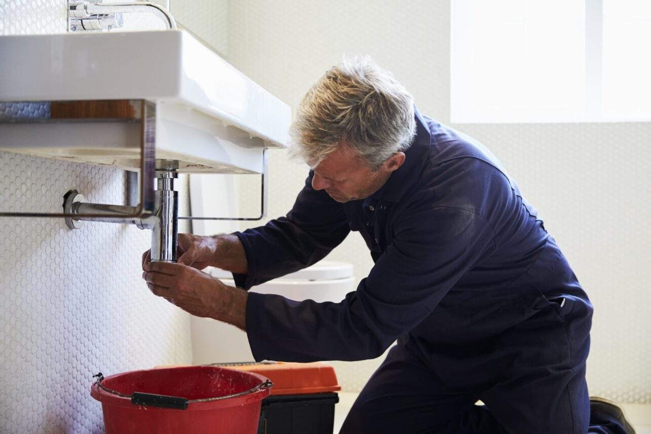 Plumber Working On Sink In Bathroom